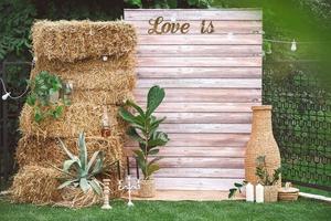 zona de foto de casamento rústico decorada com fundo de madeira, feno, vasos de vime com plantas, lâmpadas e velas. copiar, espaço vazio para texto