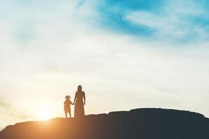 silhueta da mãe com a filha em pé e pôr do sol foto