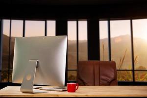 computador do espaço de trabalho colocando na mesa de trabalho de madeira e cercado por uma xícara de café, prancheta, vaso de plantas, pilha de smartphone, tablet e escritório ordenado de teclado. foto