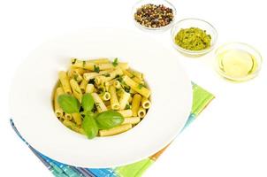 macarrão penne com molho pesto de manjericão espinafre na chapa branca. foto