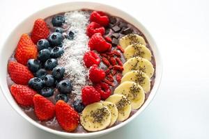 Açaí superalimentos smoothies tigela branca com sementes de chia, morango, goji berry, coco, mirtilo, coberturas de framboesa e chocolate no fundo branco foto