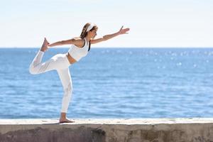jovem fazendo ioga na praia vestindo roupas brancas