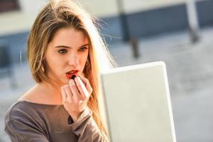 jovem mulher aplicando batom olhando para tablet foto