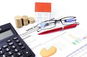 conceito de empréstimos hipotecários com pilha de moedas de dinheiro e papel de casa com óculos e caneta vermelha e calculadora foto