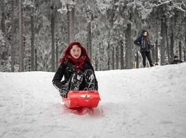 uma garota com cabelo vermelho trenós na neve do inverno na floresta. foto