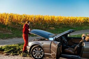 uma linda garota perto de um carro quebrado em um campo, um conversível retrô foto