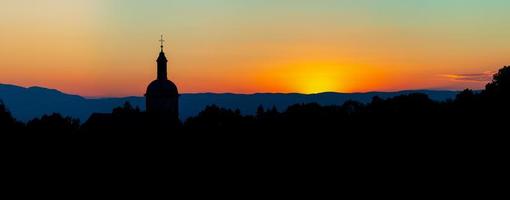 a beleza estonteante e as cores do pôr do sol com vista para as silhuetas dos alpes e a silhueta de uma bela igreja foto