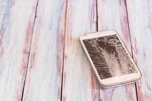 smartphone com tela quebrada na mesa de madeira foto