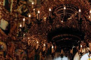 lustre folheado a ouro pendurado na antiga igreja perto dos ícones. lâmpadas modernas são como velas. foto