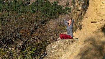 mulher com olhos fechados e braços atrás da cabeça, sentado em uma montanha na posição de lótus em meditação em um dia de outono foto