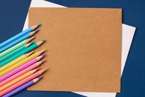 cartão de papel de vista superior com lápis pastel de cor no fundo da mesa azul marinho foto
