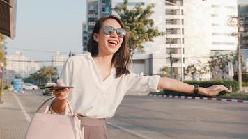 bem sucedida jovem empresária da ásia em roupas de escritório de moda saudando na estrada pegando táxi e segurando o telefone inteligente em pé ao ar livre na cidade moderna urbana. negócio em movimento conceito. foto