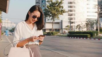 bem sucedida jovem empresária da ásia em roupas de escritório de moda saudando na estrada pegando táxi e segurando o telefone inteligente em pé ao ar livre na cidade moderna urbana. negócio em movimento conceito. foto