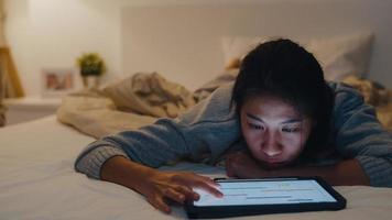 roupas casuais de mulheres asiáticas freelance usando laptop trabalho duro na cama no quarto à noite em casa. trabalhando em casa, trabalho remoto, auto-isolamento, distanciamento social, quarentena para prevenção de coronavírus. foto