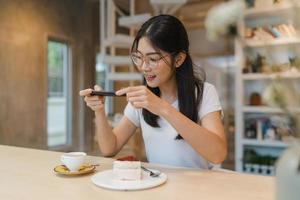 influenciador de mulheres asiáticas amigáveis blogueiros comem bolo no café noturno. linda jovem feliz relaxe divertido usando o telefone celular de tecnologia tirando uma foto de seu upload de comida nas mídias sociais no campus da faculdade.