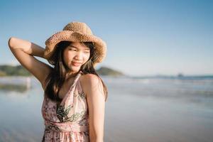 jovem mulher asiática se sentindo feliz na praia, linda fêmea feliz relaxe sorrindo divertido na praia perto do mar ao pôr do sol à noite. mulheres de estilo de vida viajam no conceito de praia. foto