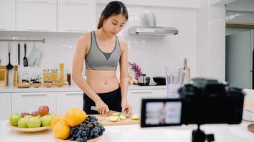 blogueira esportiva mulher asiática usando câmera gravando como fazer um vídeo de suco de maçã para seu assinante, mulher usa frutas orgânicas fazendo suco de maçã sozinha em casa. conceito de comida saudável. foto