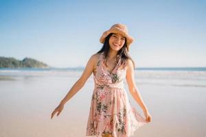 jovem mulher asiática caminhando na praia. linda fêmea feliz relaxe caminhando na praia perto do mar ao pôr do sol à noite. mulheres de estilo de vida viajam no conceito de praia. foto