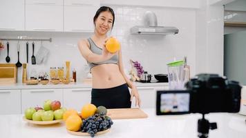 blogueira esportiva mulher asiática usando câmera gravando como fazer um vídeo de suco de laranja para seu assinante, mulher usa frutas orgânicas fazendo suco de laranja sozinha em casa. conceito de comida saudável. foto