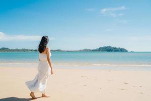 bela jovem asiática feliz relaxe andando na praia perto do mar. mulheres de estilo de vida viajam no conceito de praia. foto