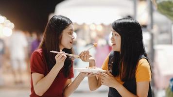 amigos de mulheres jovens asiáticas viajam em bangkok, tailândia, linda fêmea se sentindo feliz andando e comendo pad thai na estrada khao san. as mulheres viajam comem comida de rua no conceito de tailândia. foto