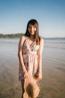 jovem mulher asiática se sentindo feliz na praia, linda fêmea feliz relaxe sorrindo divertido na praia perto do mar ao pôr do sol à noite. mulheres de estilo de vida viajam no conceito de praia. foto