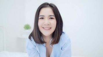 retrato mulher chinesa asiática se sentindo feliz sorrindo no quarto em casa. garota japonesa relaxa sorriso cheio de dentes olhando para a câmera enquanto estava deitado na cama no quarto em casa no conceito de manhã. foto