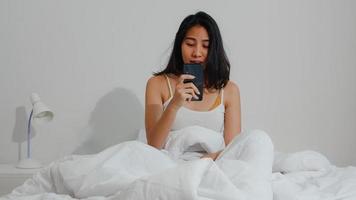jovem asiática sonolenta chocada ao acordar tarde para um compromisso na cama no quarto em casa de manhã. a mulher indiana perdeu o toque do despertador no celular e dormiu demais ao acordar. foto
