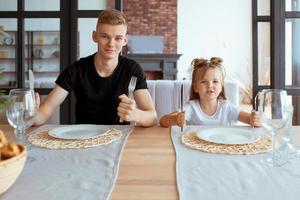 irmãos bonitos engraçados caucasianos - menina com o irmão mais velho na sala de jantar no interior do loft moderno. família, estilo de vida e conceito de alimentação foto