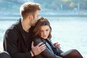 lindo incrível engraçado alegre jovem casal abraçando ao ar livre à beira do rio no fundo da ponte. namorada e namorado. conceito de família, amor e amizade foto