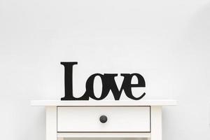 letras pretas amam de uma árvore em uma mesa branca. cortar a letra de madeira. letras de amor em um fundo branco foto