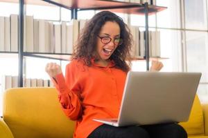 mulher latina trabalhando com laptop no sofá e sentindo-se feliz foto