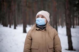 garota loira atraente com uma máscara médica está andando na floresta. foto