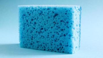 uma esponja azul usada para lavar e apagar a sujeira usada pelas donas de casa no dia a dia. eles são feitos de material poroso, como espuma. retenção de detergente, o que permite gastá-lo economicamente foto