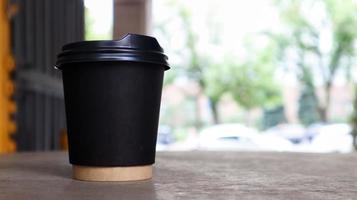 copo de papel preto sem texto e logotipo com café com tampa plástica em uma mesa de madeira de um café de rua na cidade. copie o espaço. foto