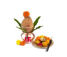 kalash de cobre com coco e folha de manga e pooja thali com diya, kumkum e doces com decoração floral em um fundo branco. essencial no puja hindu. foto