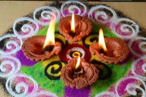 lâmpadas diya de argila acesas durante a celebração do diwali, rangoli ao fundo foto