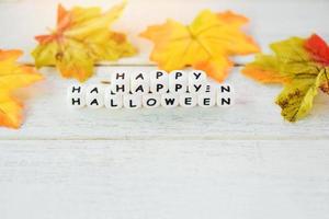 fundo de halloween com blocos de palavras decorações de halloween felizes e folhas de outono no conceito de férias de mesa de madeira branca foto