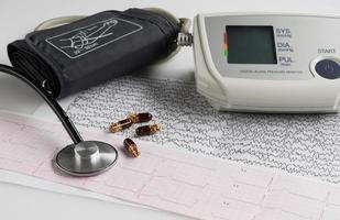 tonômetro elétrico moderno e um estetoscópio em um gráfico de eletrocardiograma. monitor de pressão arterial doméstico foto