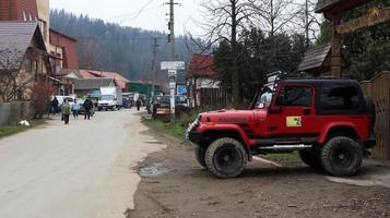 ucrânia, yaremche - 20 de novembro de 2019. um jeep wrangler vermelho 4.0i v6 suv está estacionado em uma estrada rural perto de uma casa em uma pequena cidade de cárpatos ucranianos. excursões passeio de jipe na montanha. foto