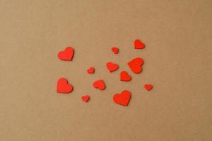 muitos pequenos corações vermelhos de madeira em um fundo de papel kraft. fundo de amor, conceito de dia dos namorados foto
