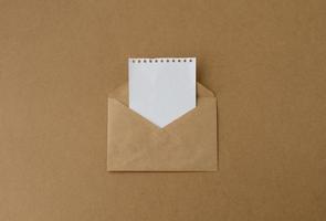 envelope marrom com um cartão branco em branco, um envelope de papel kraft com uma folha branca de um notebook foto