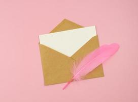 cartão em branco, envelope de correio vintage e pena rosa em fundo rosa. carta de amor, mensagem romântica foto