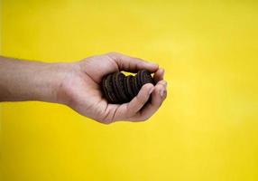 mãos segurando biscoitos de chocolate em um fundo amarelo com espaço de cópia foto