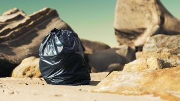 saco de lixo plástico preto cheio de lixo na praia foto