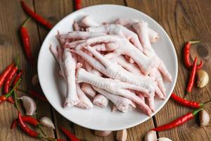 pés de frango na chapa branca com ervas e especiarias pimenta alho, pés de frango cru fresco para sopa de comida cozida no fundo da cozinha de mesa de madeira foto