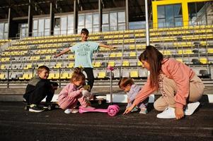 jovem mãe elegante com quatro filhos ao ar livre. família de esportes passa o tempo livre ao ar livre com patinetes e patins. pintado com giz no asfalto. foto