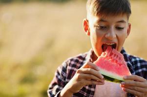 menino adolescente usa camisa quadriculada com aparelho nos dentes, come melancia. foto