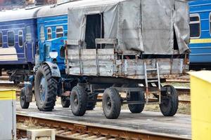 um velho trator com um reboque de madeira e um estande anda em uma plataforma ferroviária. foto