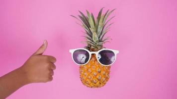 fruta de abacaxi com óculos e polegar isolado no fundo rosa foto